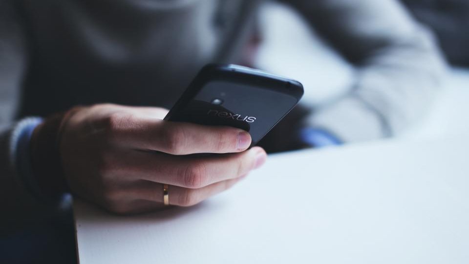Due mani tengono uno smartphone acceso in una stanza buia