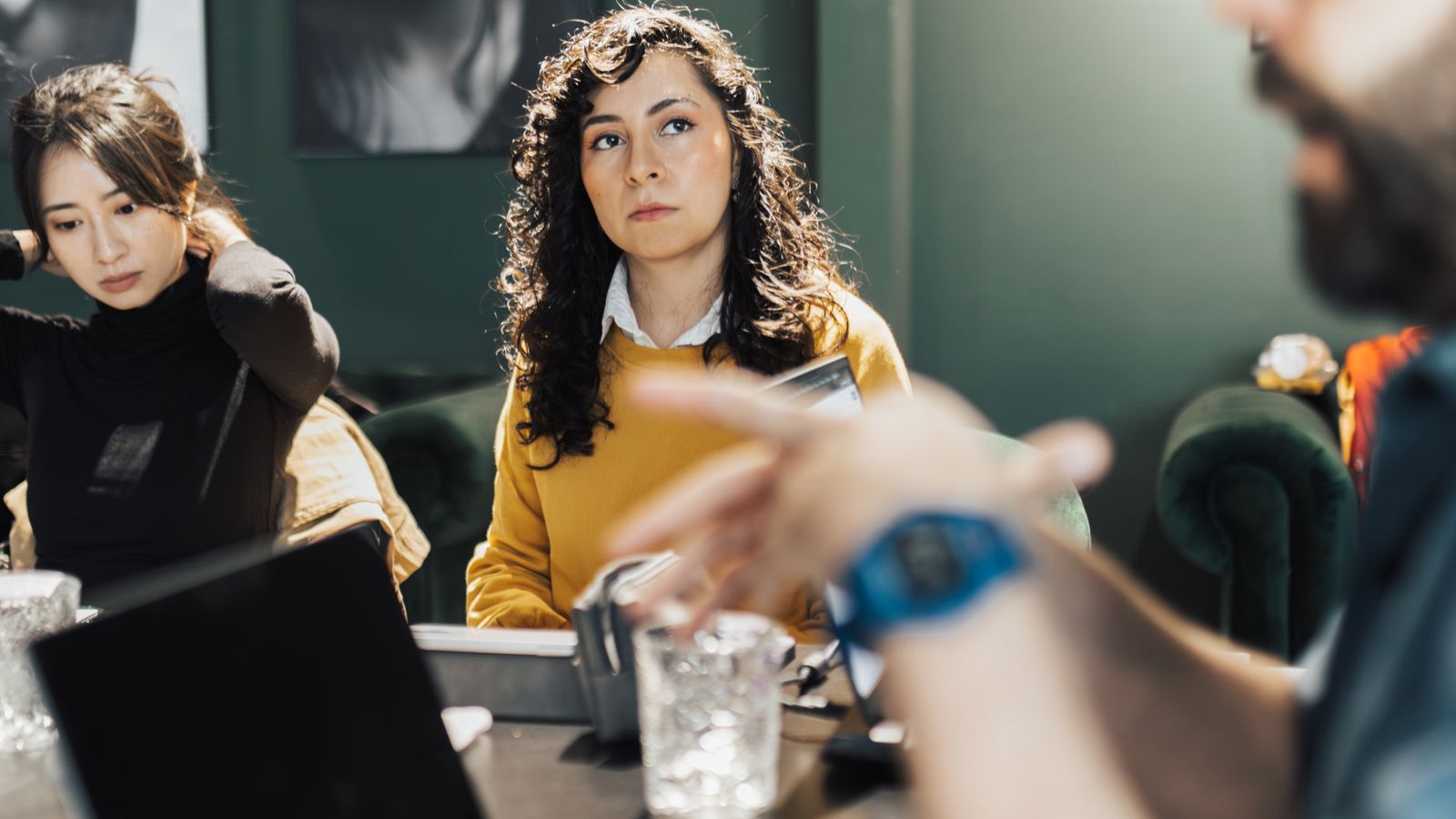Tre colleghi attorno a un tavolo di lavoro discutono un progetto, con un portatile aperto