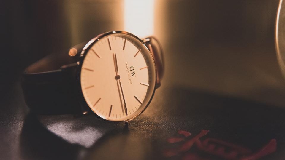 Un orologio da polso con il quadrante chiaro appoggiato su una scrivania scura